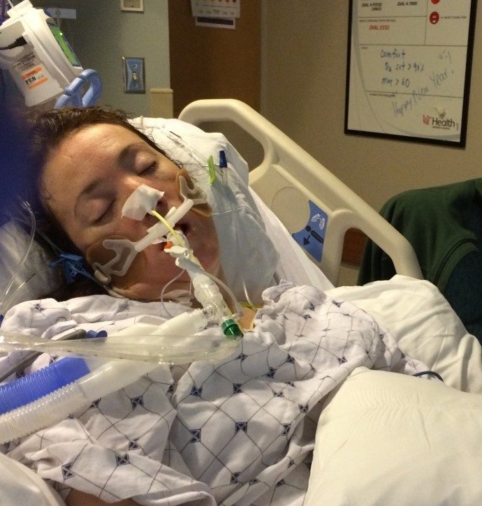Rebecca asleep in an ICU bed on a ventilator, with a handwritten Happy New Year message on a whiteboard behind her.