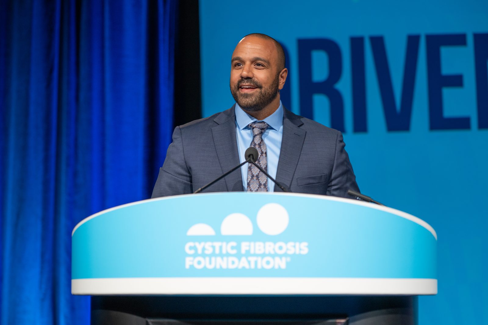 Ray Poole smiling at a podium with the Cystic Fibrosis Foundation logo.